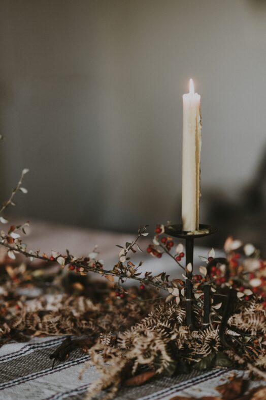 Ett tänt stearinljus på en ljusstake omgiven av torkade blommor.