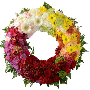En blomsterkrans arrangerad i olika färgade sektioner med vita, gula, orange, röda och lila blommor, omgiven av gröna blad.